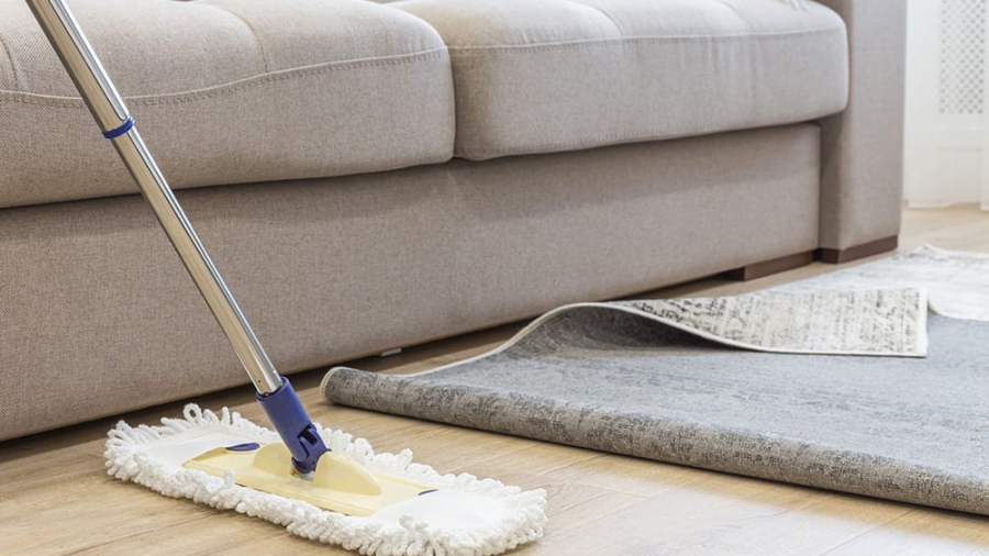 Cleaning floor with mop under carpet in living room, concept of good cleaning service